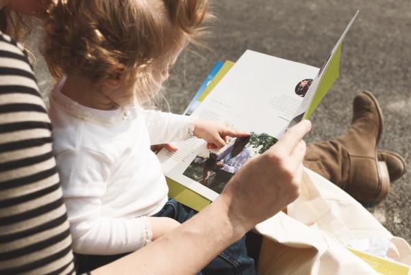 Child sitting on her mother's lap reading in a brochure by aspern Seestadt